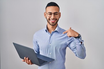 Wall Mural - Young hispanic man working using computer laptop looking confident with smile on face, pointing oneself with fingers proud and happy.