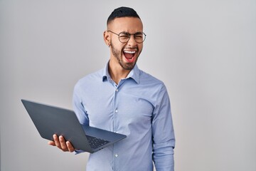 Poster - Young hispanic man working using computer laptop angry and mad screaming frustrated and furious, shouting with anger. rage and aggressive concept.