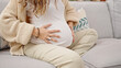 © Krakenimages.com - Young pregnant woman sitting on sofa massaging belly at home