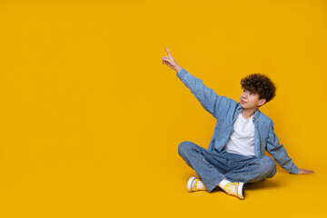 Wall Mural - Teenager pointing finger up on yellow background