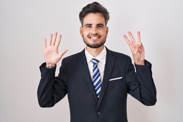 Sticker - Young hispanic man with tattoos wearing business suit and tie showing and pointing up with fingers number eight while smiling confident and happy.