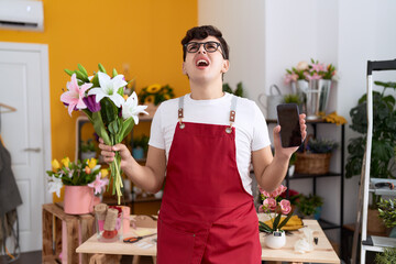 Sticker - Young non binary man working at florist shop showing smartphone screen angry and mad screaming frustrated and furious, shouting with anger looking up.