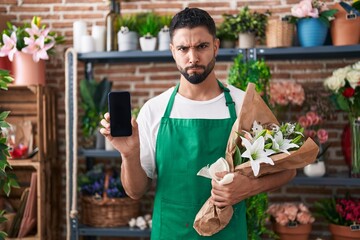 Wall Mural - Hispanic young man working at florist shop showing smartphone screen skeptic and nervous, frowning upset because of problem. negative person.