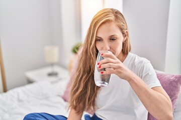 Sticker - Young blonde woman drinking glass of water sitting on bed at bedroom