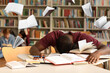 © Pixel-Shot - Tired African-American student preparing for exam in library with flying books