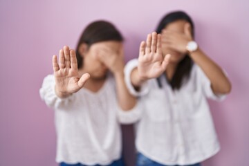 Wall Mural - Hispanic mother and daughter together covering eyes with hands and doing stop gesture with sad and fear expression. embarrassed and negative concept.