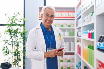 Poster - Middle age grey-haired man pharmacist using smartphone working at pharmacy