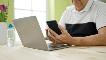 Canvas Print - Middle age man with grey hair using smartphone and laptop at dinning room