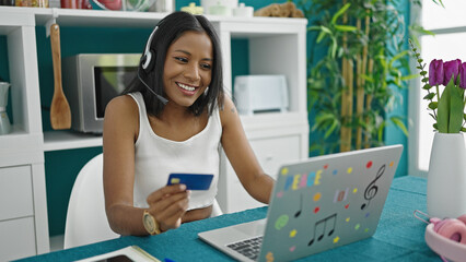 Wall Mural - African american woman having video call holding credit card at dinning room