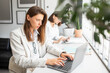 © Prostock-studio - Female office manager working on laptop in coworking space, colleague using digital tablet sitting at desk on background
