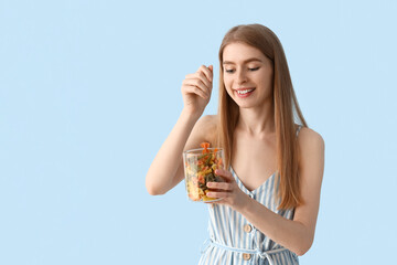 Wall Mural - Young woman with jar of raw pasta on blue background