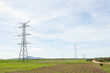 © Mer - High voltage power lines and pylons in a flat green and partly plowed agricultural landscape, on a sunny day with clouds in the blue sky. Horizontal