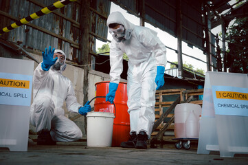 Specialist Officers in Chemical Safety Wear Chemical Risk Protective Clothing Hand Raised Saying Caution for Chemical Spill while Cleanup and Recovery in Carrying a Bucket in Part of Chemical Spills.