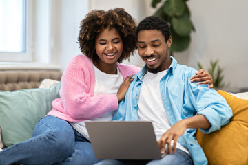 Portrait of loving african american spouses using laptop at home