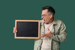 Angry male teacher with chalkboard on green background