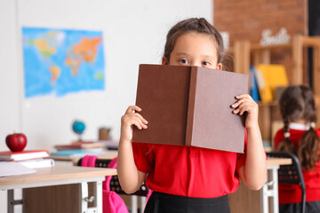 Little schoolgirl with book in classroom