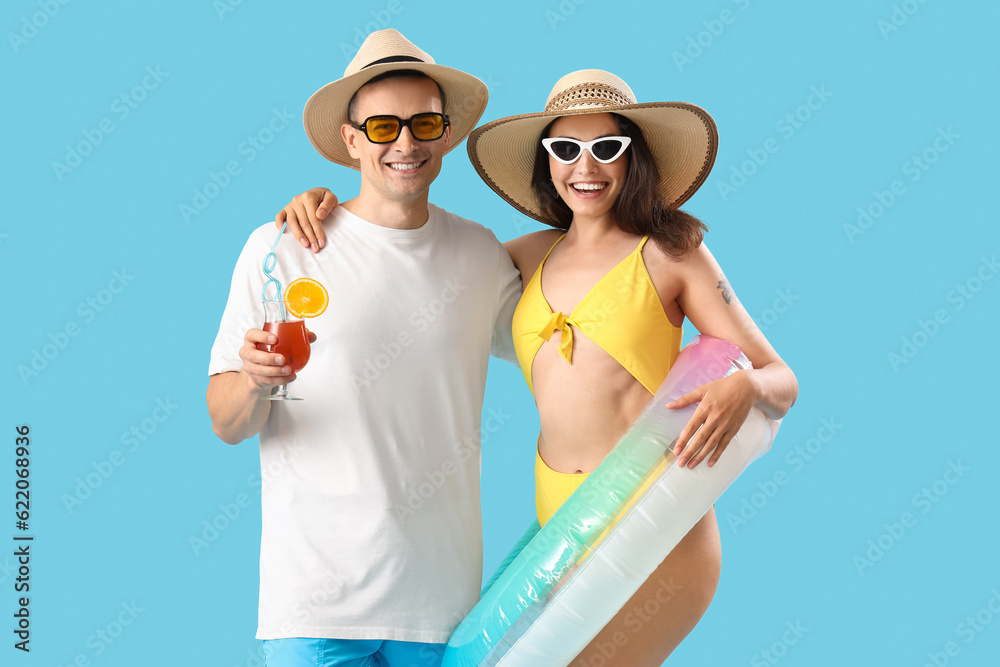 Young couple with inflatable ring and cocktail on blue background