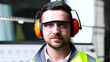© ihorvsn - Close up of handsome Caucasian man in headphones and goggles near controlling point computer, turning face and smiling to camera. Inside. Portrait of male in yellow uniform at producing plant.
