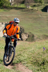 Sticker - Young man cycling on a rural road through green spring meadow during sunset