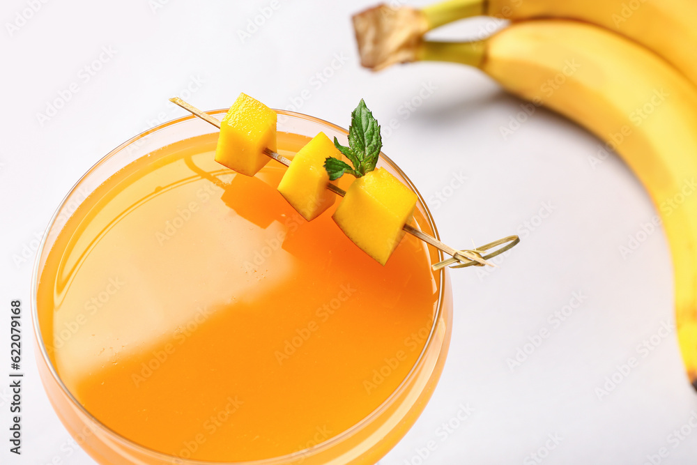 Glass of fresh mango juice and bananas on white background