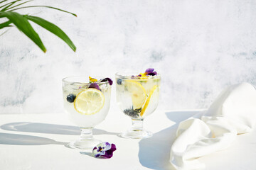 Wall Mural - Cold water with lemon garnished with edible flowers. Cool summer lemonade. Summer non-alcoholic cocktails and drinks.