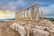 The Temple of Poseidon, an ancient Greek temple on Cape Sounion, Greece, dedicated to the god Poseidon, with the Aegean sea and coastline seen under early sunset dramatic skies.
