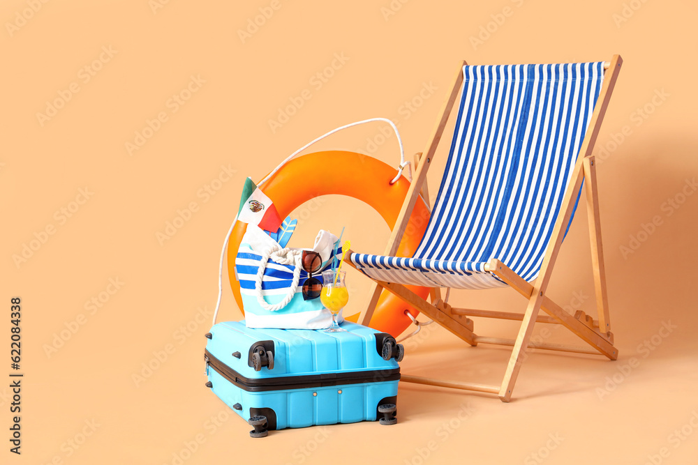 Deckchair with suitcase, ring buoy and beach accessories on beige background. Travel concept