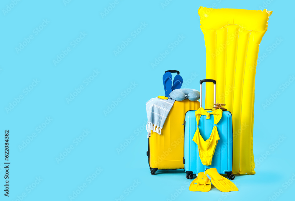Suitcases with inflatable mattress and different beach accessories on blue background. Travel concept