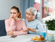 Careful loving elderly mother comforting her upset adult daughter at home table.