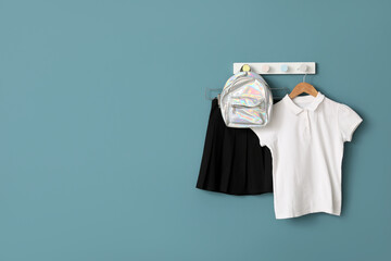 Stylish school uniform and backpack hanging on color wall