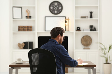 Poster - Home workplace. Man working at wooden desk in room, back view