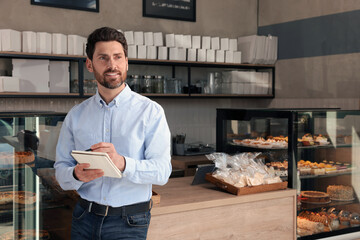 Happy business owner with notebook and pen in bakery shop