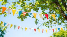 Colorful Pennant String Decoration In Green Tree Foliage On Blue Sky, Summer Party Background Template Banner With Copy Space
