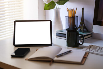 Modern workspace with a tablet computer, pot plant, notebook and coffee cup on white desk. Blank screen monitor for graphic display montage.
