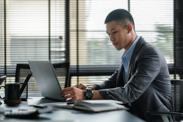 Gorgeous young businessman sitting in bright office and looking at computer laptop screen.