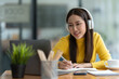 © Phimwilai - Asian female student or office worker studying online using headphones and laptop taking notes in notebook sitting at coffee shop table relaxing and changing places to work relax.