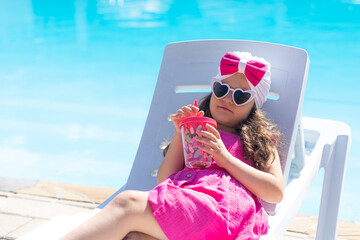 Wall Mural - Little cute girl lying on a beach lounger chair by the pool and drinking lemonade. Relaxation resting vacations concept. Summer vacation. high quality