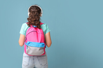 Wall Mural - Female student in headphones with backpack on blue background, back view