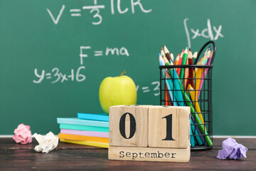 Different stationery, fresh apple and calendar with date SEPTEMBER 1 on wooden table against green chalkboard