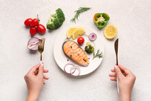Woman eating tasty grilled salmon steak with vegetables on light background