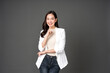 Asian female executive with long hair Poses with raised hands pointing fingers beautiful smile Wearing a white suit and jeans, excited faces, bright, Take a photo in the gray background studio