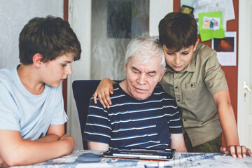 Two Preteen Boys Teaching Grandfather How to Use Internet Safely. Teenage Brothers, School Children with Digital Tablet Playing with Granddad, Senior Man at Home.