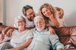 © luciano - Happy bonding family group relaxing on sofa at home having fun and laughing. Handsome people, parents and adult sons, two generations looking at camera