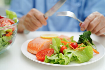 Asian elderly woman patient eating salmon stake and vegetable salad for healthy food in hospital.