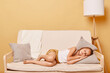 © sementsova321 - Full length of sleeping little girl lying on a couch with hand under cheek keeps eyes closed resting at home day napping relaxing during free time.