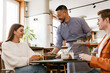 © Drobot Dean - Smiling waiter serving couple in cafe