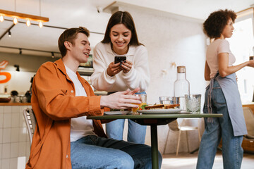 Wall Mural - Couple using mobile phone while having lunch together in cafe