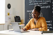 © Mediaphotos - Young African American teacher working online on laptop while sitting in the classroom