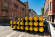 Black insulated pipes with yellow plastic plugs stacked on a city street. Old buildings and blue sky.