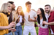 © CarlosBarquero - Multi-ethnic friends chatting over a bottle of beer outdoors. Group of young diverse people standing party drinking bottled beer talking and laughing in city park. Concept of hanging out in community
